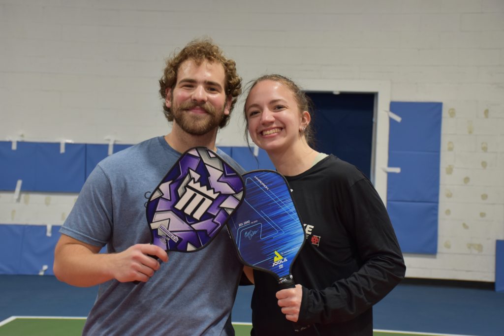 Marie and Tyler posing for a photo with their pickleball paddles.